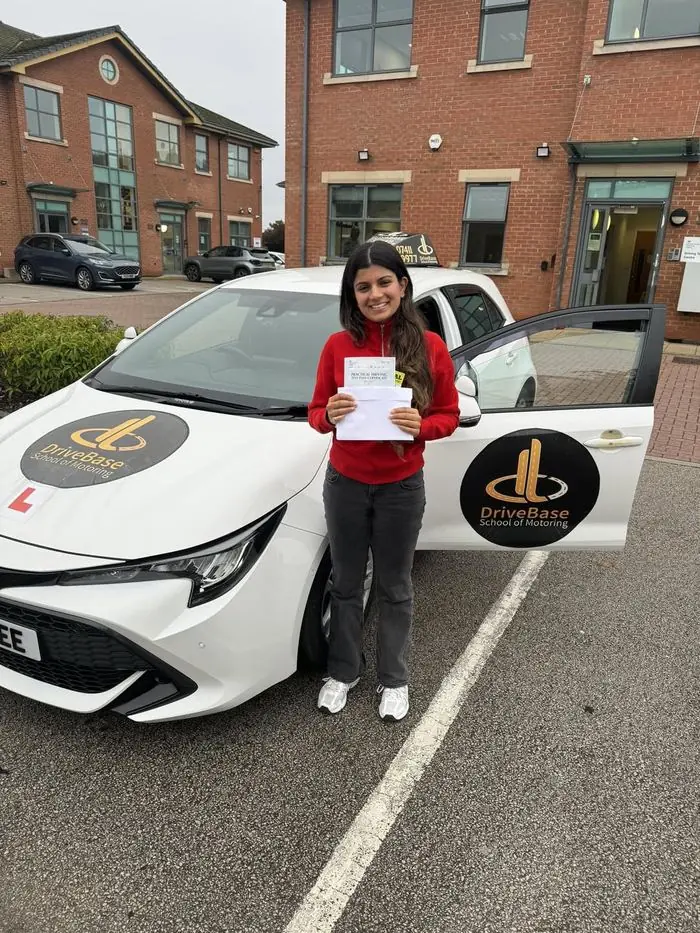 Dr Samira with their driving test pass certificate beside the DriveBase car